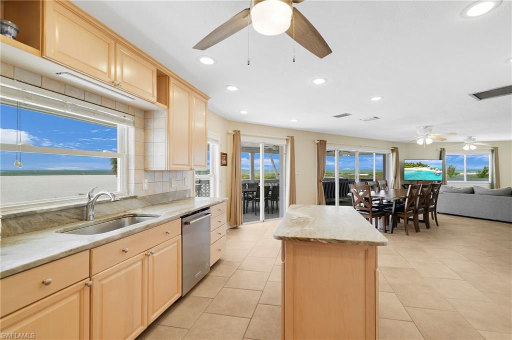 Open concept kitchen and living area featuring light-toned cabinetry, light-toned countertops, a stainless steel sink, and a built-in stainless steel dishwasher - Virtually Edited Image