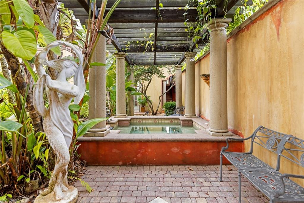Outdoor patio featuring a water feature, overhead pergola with climbing greenery, paver flooring, and stucco walls