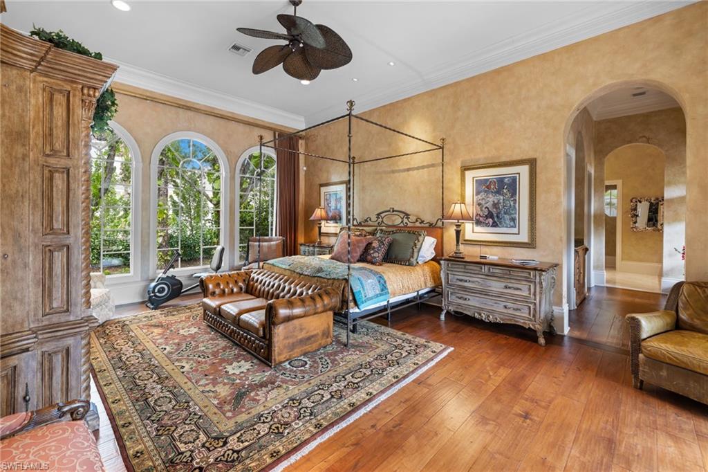 Hardwood flooring in a room featuring three arched windows, crown molding, an ornate ceiling fan, and arched doorways