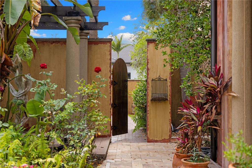 Garden pathway featuring pavers, a decorative wooden gate, stucco walls, and a wooden pergola with columnar supports