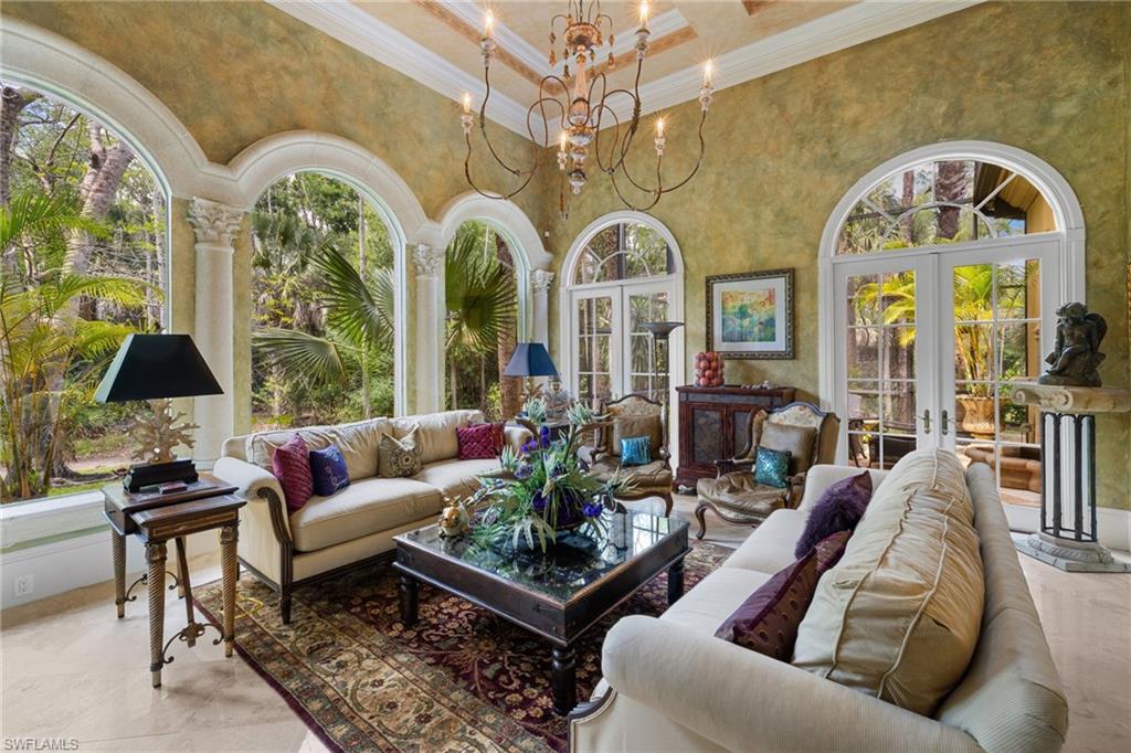 Spacious living area featuring arched windows and French doors, high ceilings with an ornate chandelier, textured wall finishes, and light-toned flooring