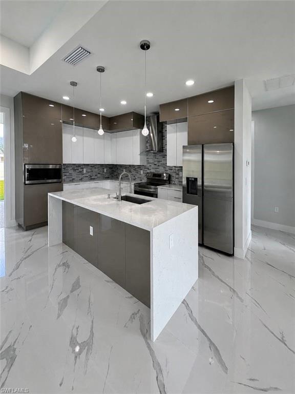 Modern kitchen featuring a waterfall island, stainless steel appliances, sleek cabinetry, pendant lighting, and large format tile flooring