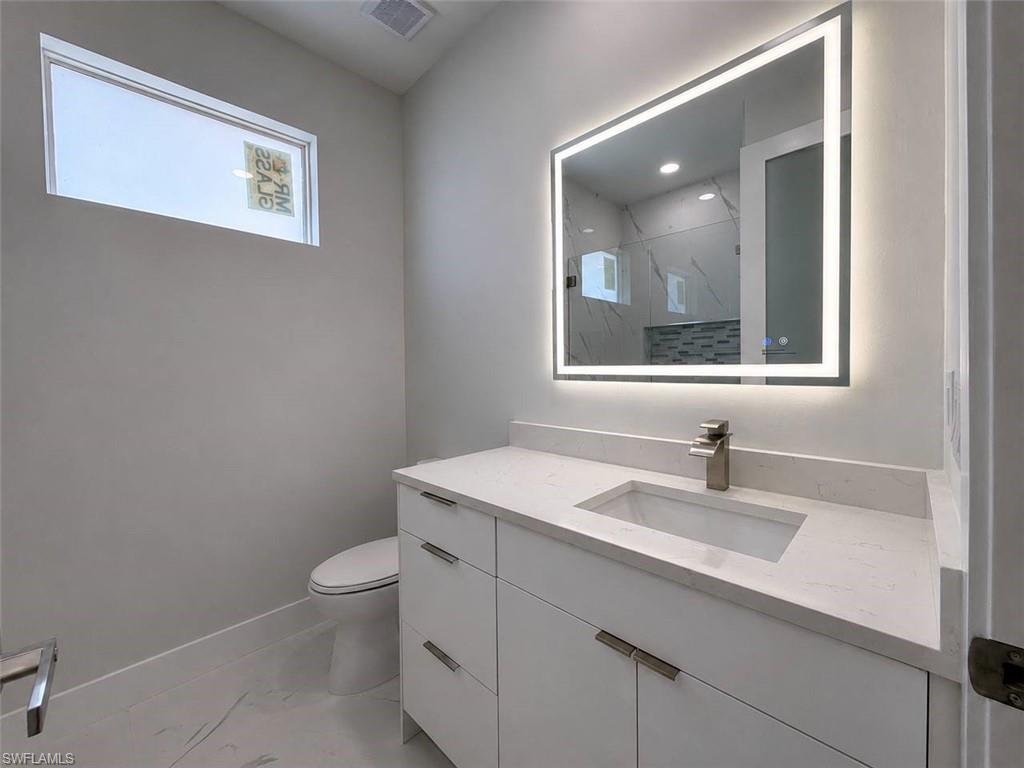 Contemporary bathroom featuring a white vanity with integrated sink, a brushed nickel faucet, and a backlit LED mirror