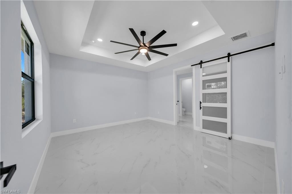 Spacious room featuring a tray ceiling with recessed lighting, a modern ceiling fan, and large format tile flooring
