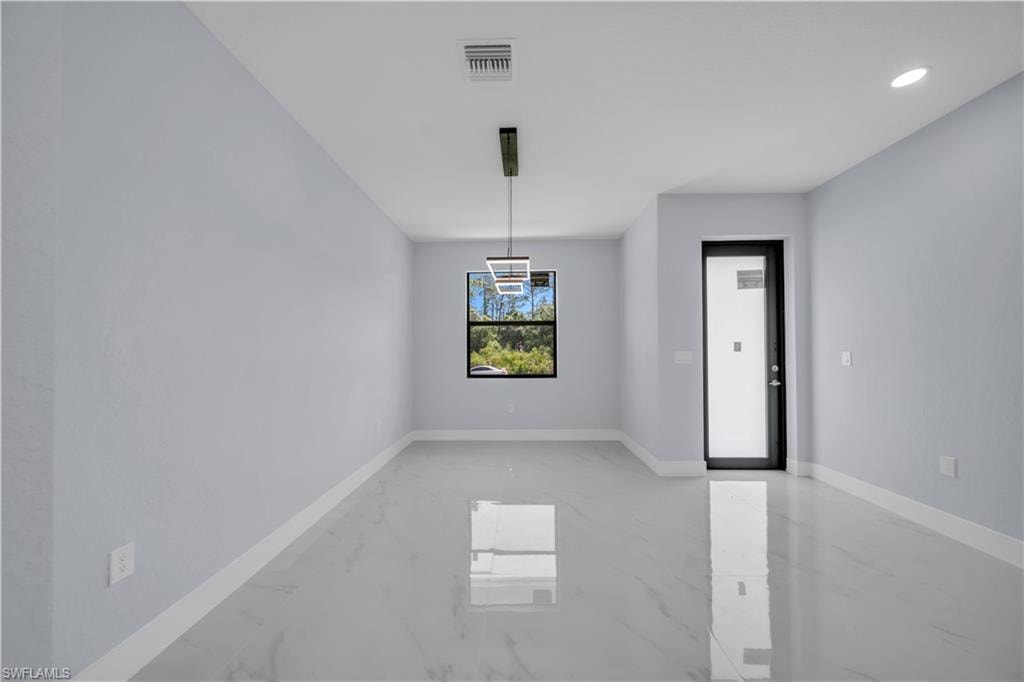 Spacious room featuring light-toned walls, contemporary lighting fixtures, and large format tile flooring