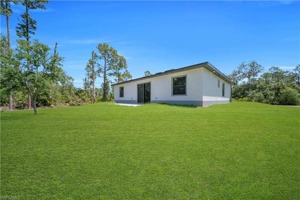 Expansive green lawn surrounds a contemporary white stucco residence with dark-trimmed windows and sliding glass doors