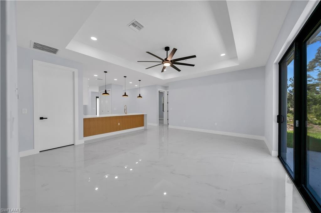 Spacious room featuring large format tile flooring, a tray ceiling with recessed lighting and a contemporary ceiling fan, and a wide sliding glass door