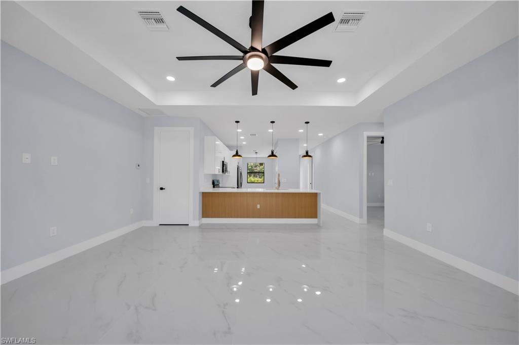 Spacious room featuring tray ceilings with a contemporary ceiling fan, recessed lighting, and glossy light-toned flooring