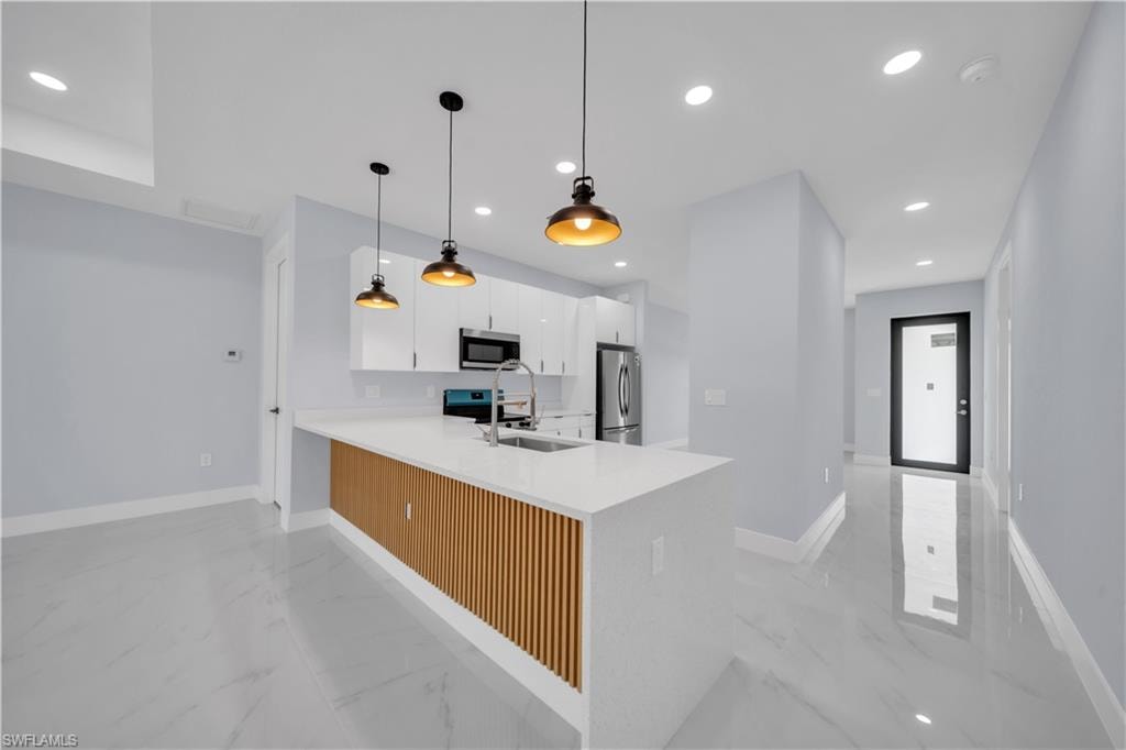 Open-concept kitchen featuring an island with a white countertop and wood-slat detailing, white flat-panel cabinetry, stainless steel appliances, and industrial-style pendant lighting
