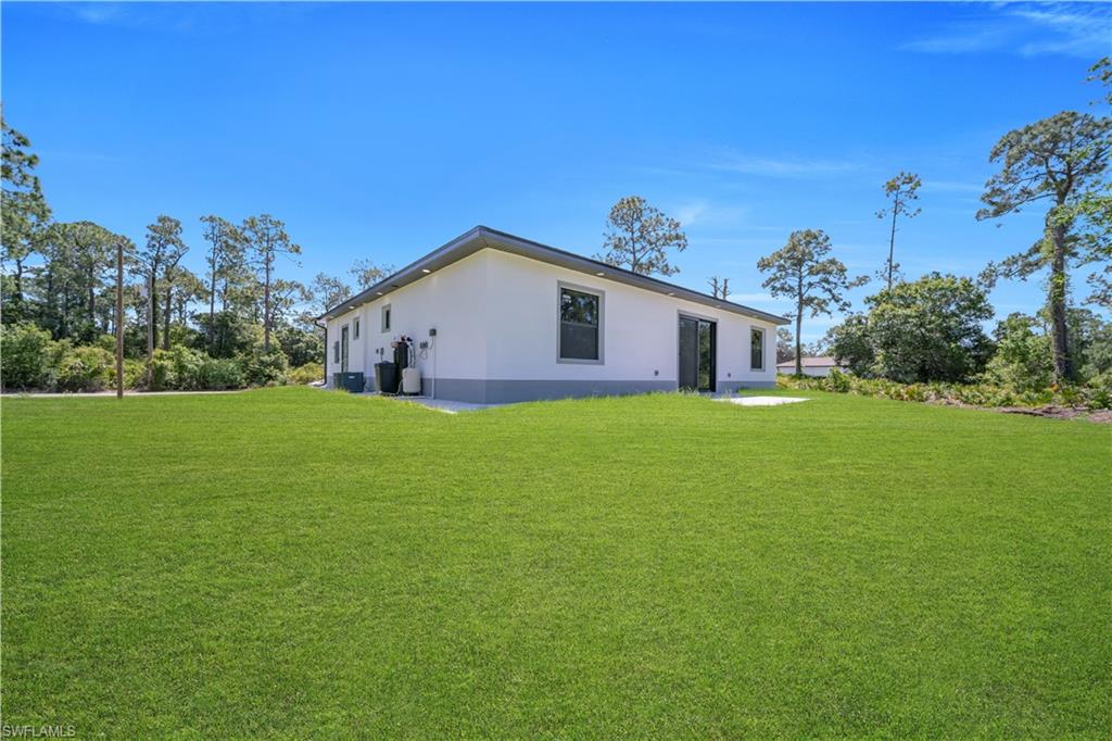 Expansive green lawn surrounds the residence, featuring a white stucco exterior with gray trim