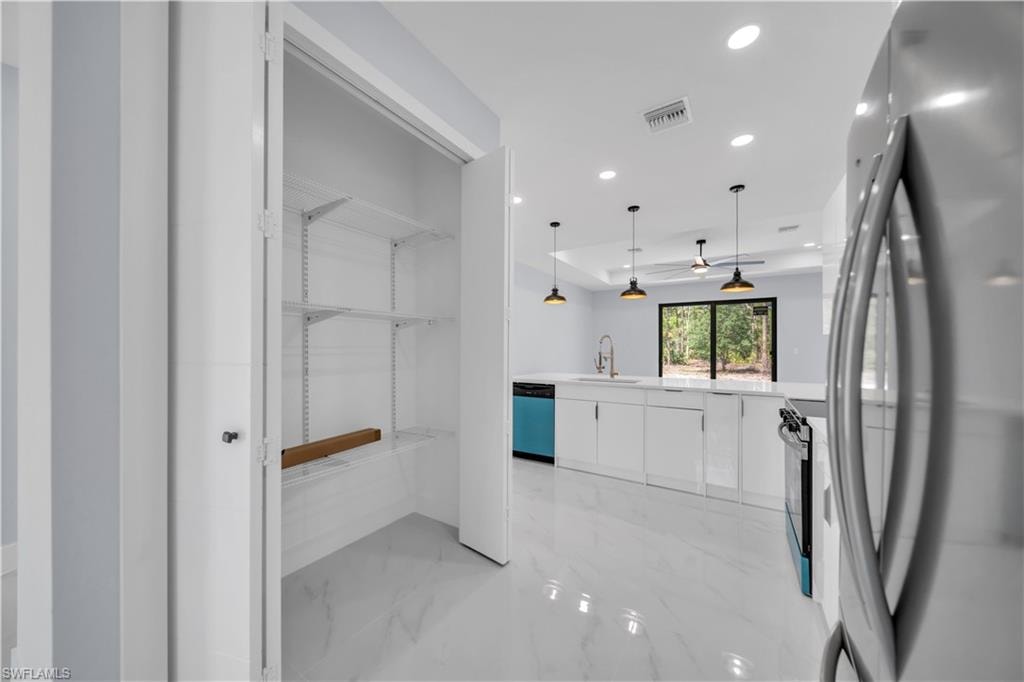 Kitchen pantry with adjustable shelving, showcasing a modern open-concept kitchen with white cabinetry, light countertops, and recessed lighting