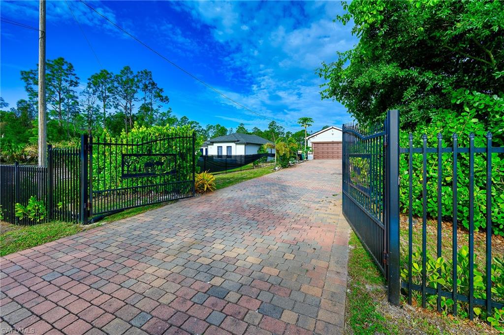 Gated entry with a multi-toned paver driveway, leading to a property featuring a white and dark-accented residence with a two-car garage