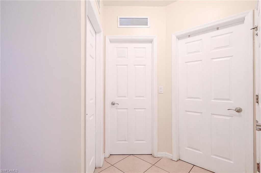 Entryway featuring light-toned tile flooring, white paneled doors with brushed nickel hardware, and a ceiling-mounted ventilation grate