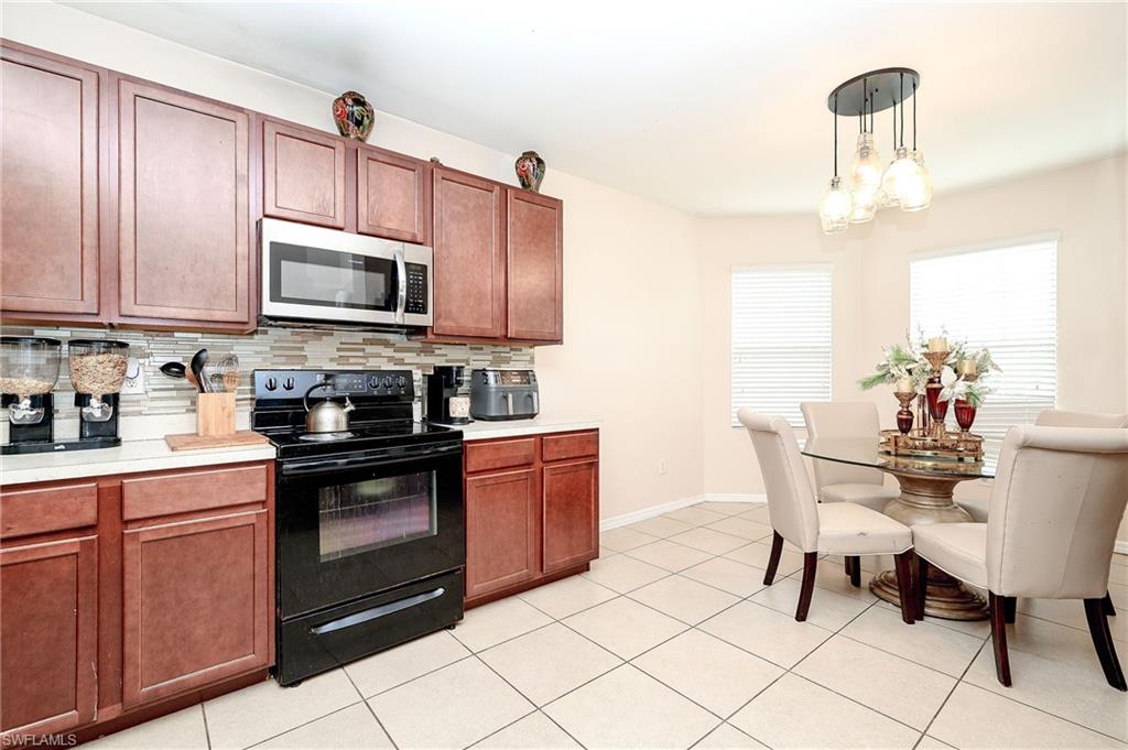 Kitchen featuring wood-finish cabinetry, stainless steel microwave, black electric range, and a mosaic tile backsplash