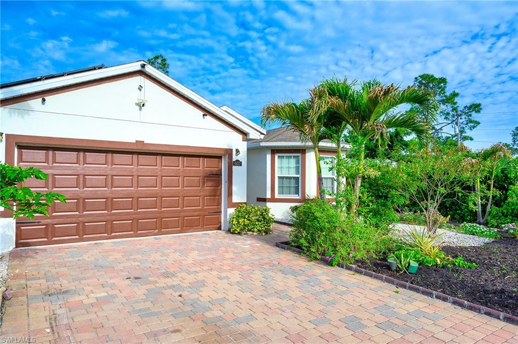 White exterior featuring a two-car garage with a panel door, paver driveway, and mature tropical landscaping