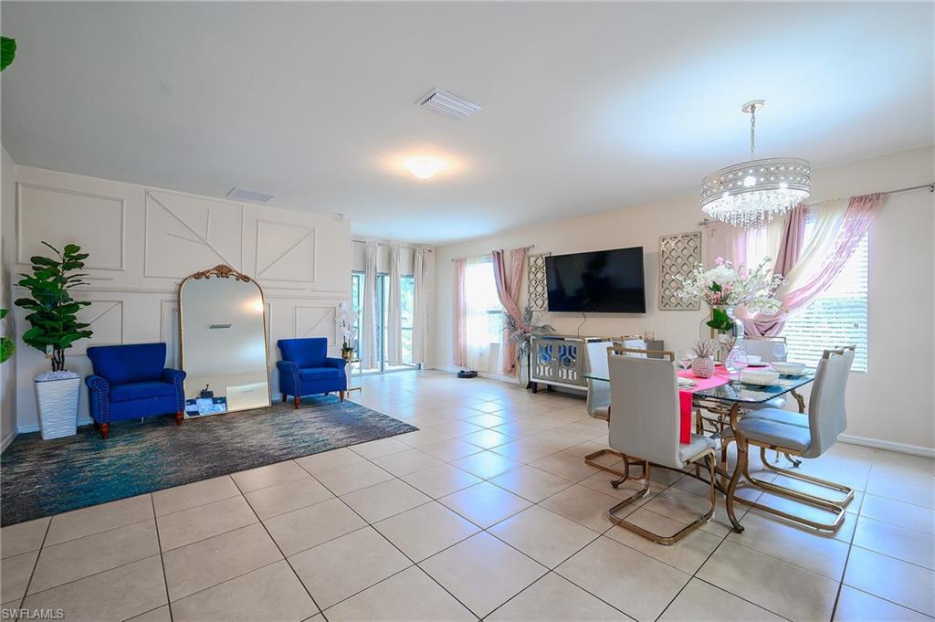 Open concept living and dining area featuring light-toned tile flooring, decorative wall paneling, and a contemporary chandelier