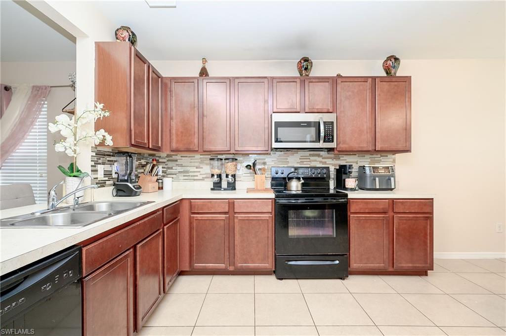 Kitchen featuring wood-finish cabinetry, light-colored countertops, a stainless steel microwave, and a black range