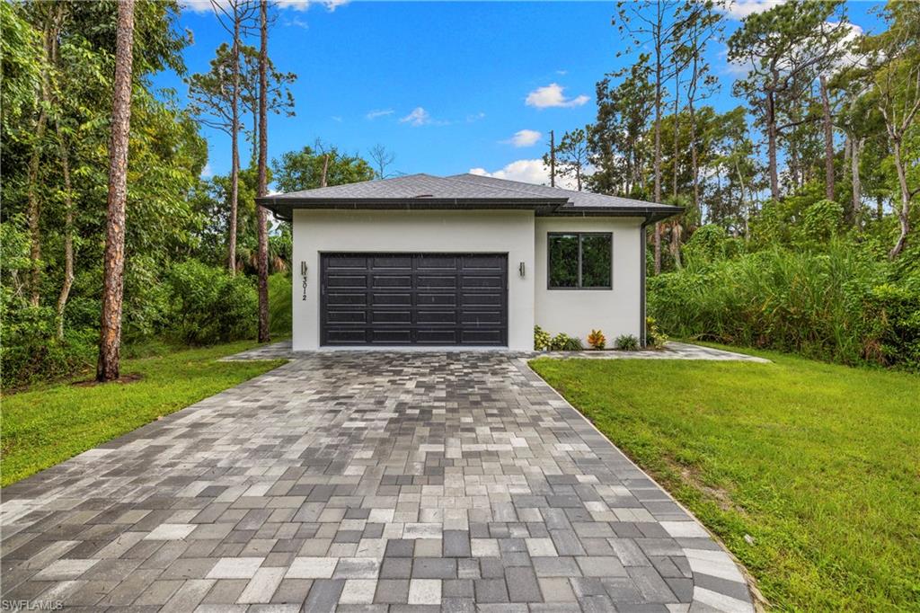 Contemporary single-story residence featuring a gray garage door, white stucco exterior, and black-framed windows
