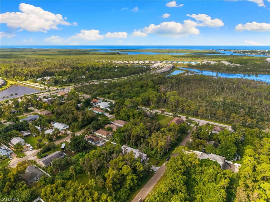 Aerial perspective highlighting abundant mature trees, residential structures, a freshwater lake, a major roadway, and distant coastal waters