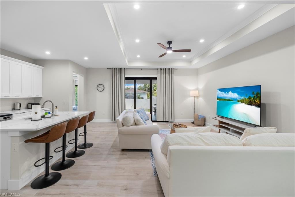 Open-concept living area with wood-finish flooring, recessed lighting, and a tray ceiling