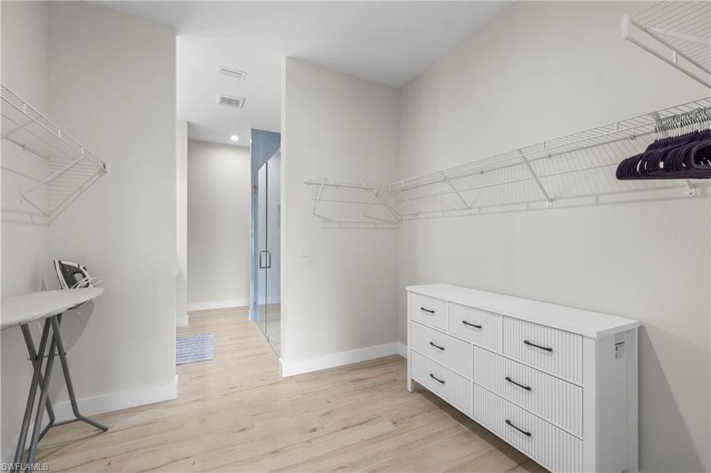 Spacious walk-in closet featuring light wood-finish flooring, white walls, and extensive wire shelving systems