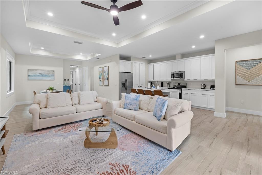 Open-concept living area with wood-finish flooring, a tray ceiling, and recessed lighting