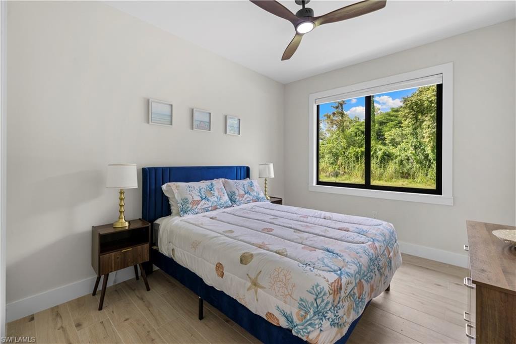 Spacious room featuring light wood-finish flooring, a contemporary ceiling fan, and abundant natural light from a large window