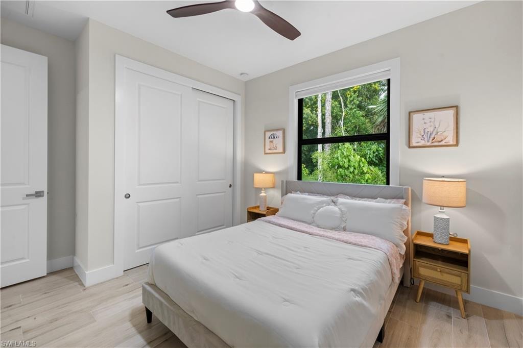Bedroom featuring light wood-finish flooring, a contemporary ceiling fan, a window overlooking trees, white panel doors, and a double-door closet with sliding panels
