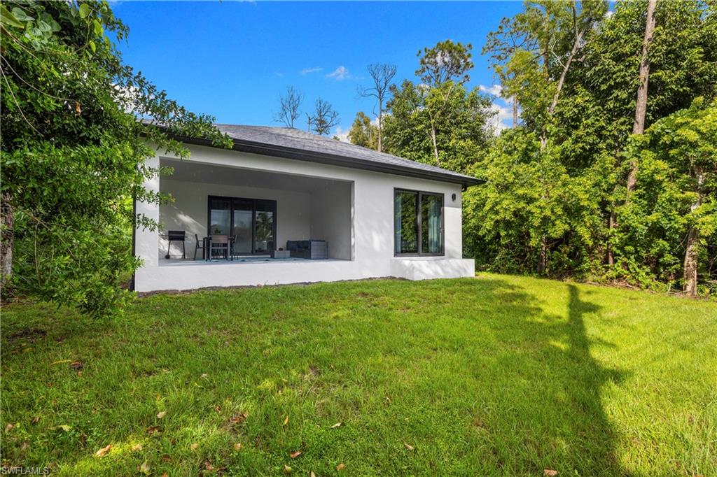 Contemporary rear exterior featuring a spacious covered patio, sliding glass doors, large window, and expansive green lawn surrounded by mature trees