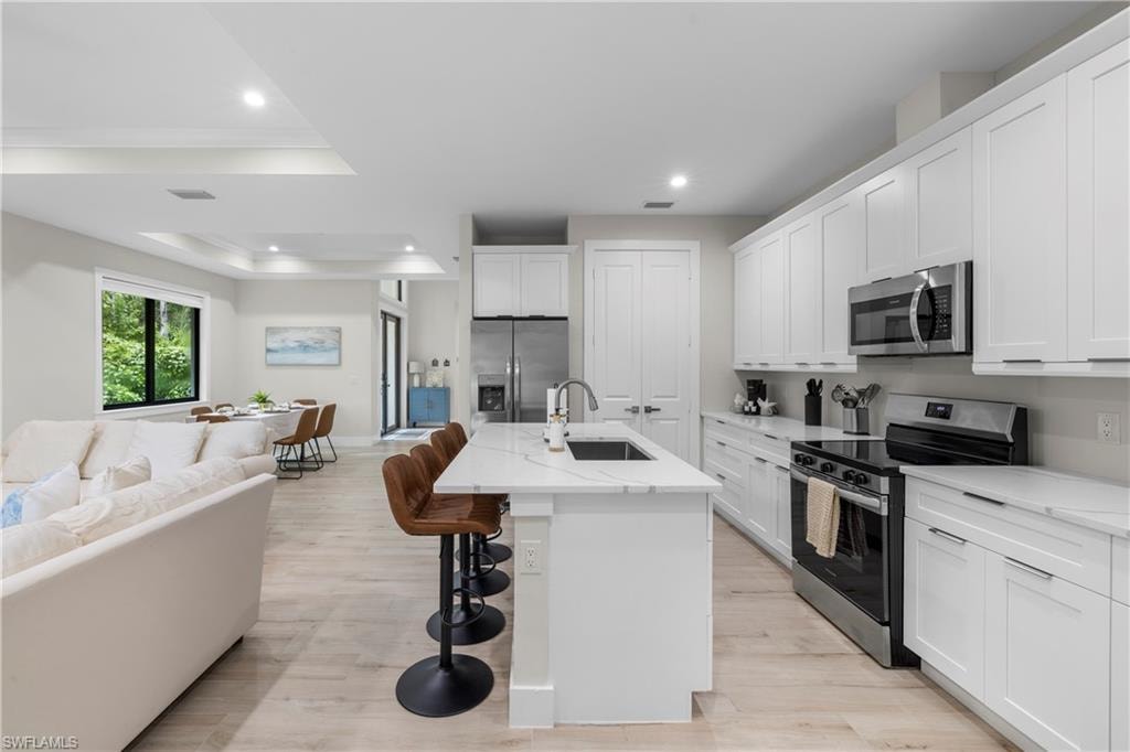 Modern kitchen featuring white shaker cabinetry, stainless steel appliances, a center island with sink and seating, and light wood-finish flooring