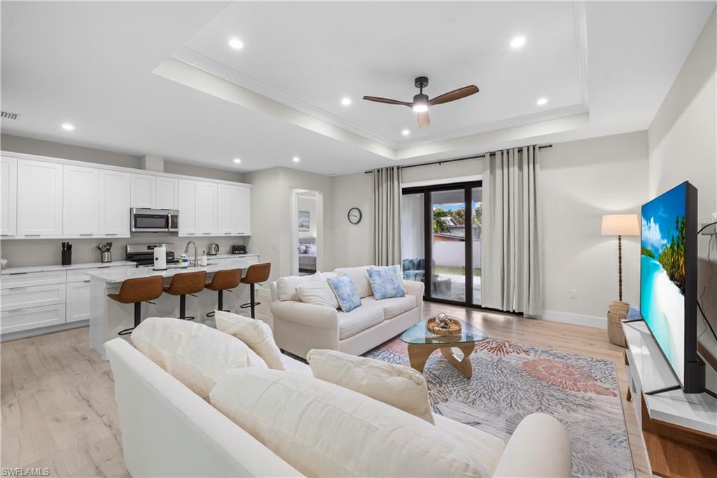 Open-concept living space featuring wood-finish flooring, a tray ceiling with recessed lighting, and a contemporary ceiling fan