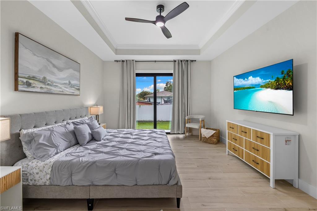 Spacious bedroom featuring wood-finish flooring, a tray ceiling with a modern ceiling fan, and direct access to the exterior through sliding glass doors