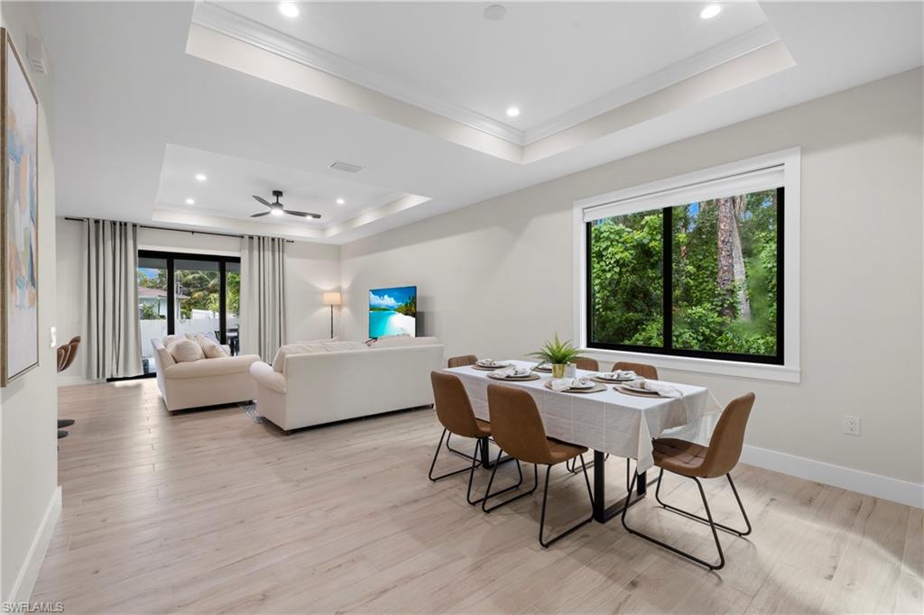 Open-concept living and dining area featuring light wood-finish flooring, a tray ceiling with recessed lighting, and a modern ceiling fan
