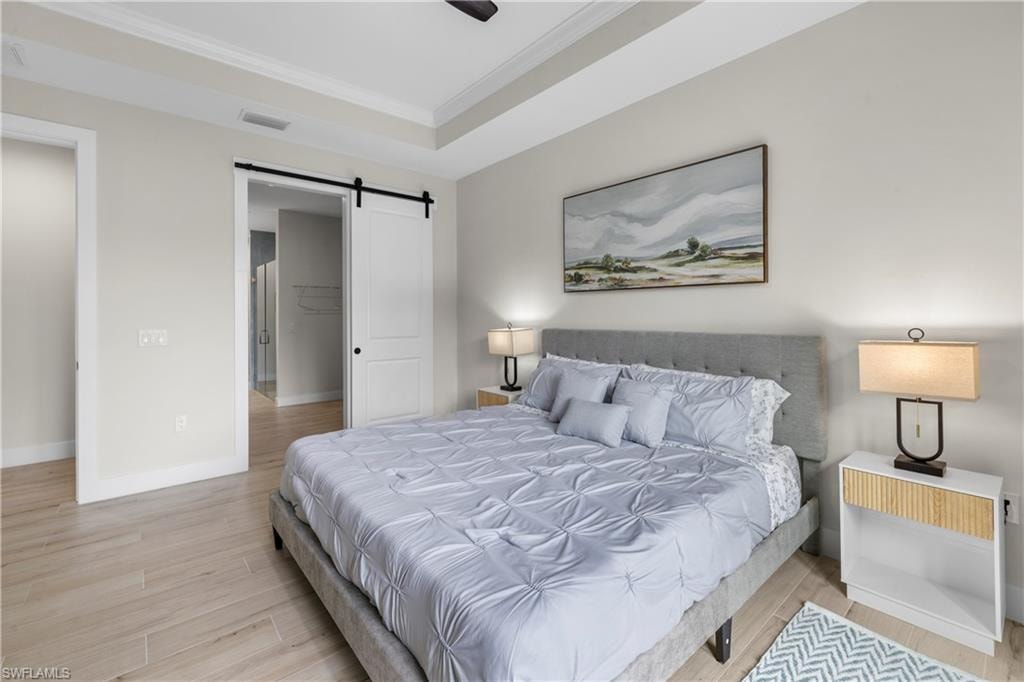Recessed ceiling with crown molding, wood-finish flooring, and a modern barn door