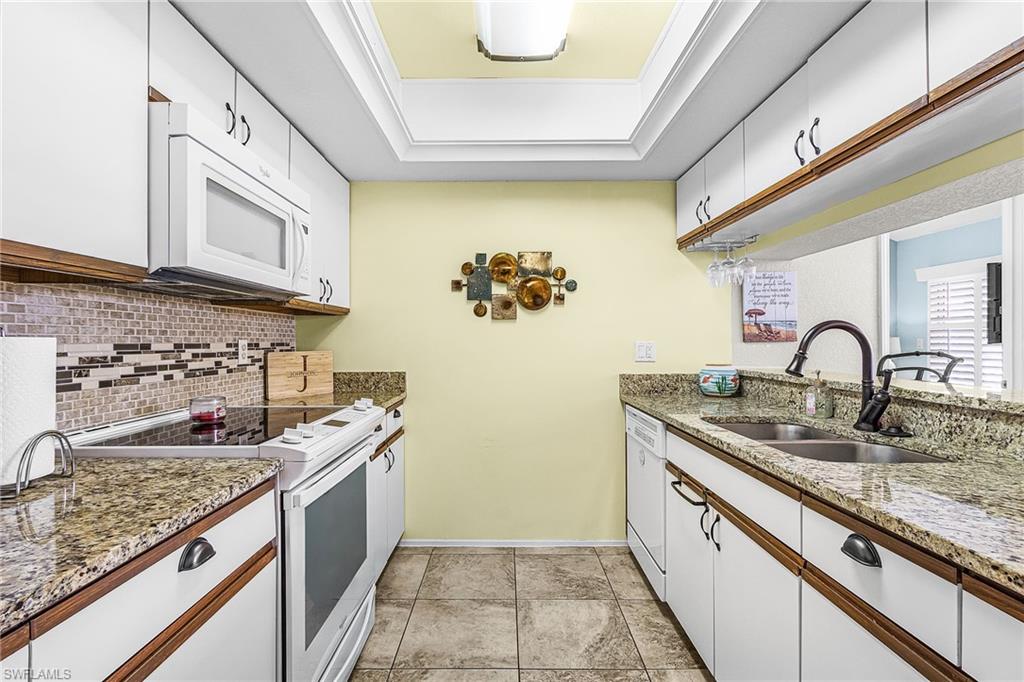 Kitchen featuring white appliances, white cabinets, light stone counters, decorative backsplash, and light tile floors