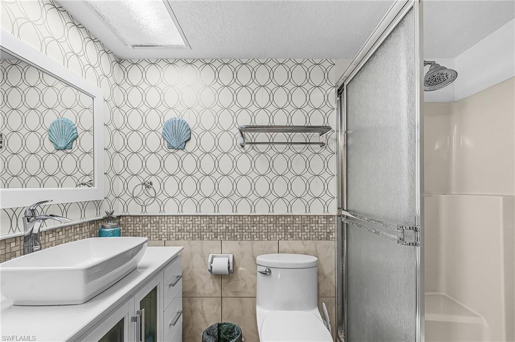 Full bathroom with tile walls, vanity, a stall shower, and a textured ceiling