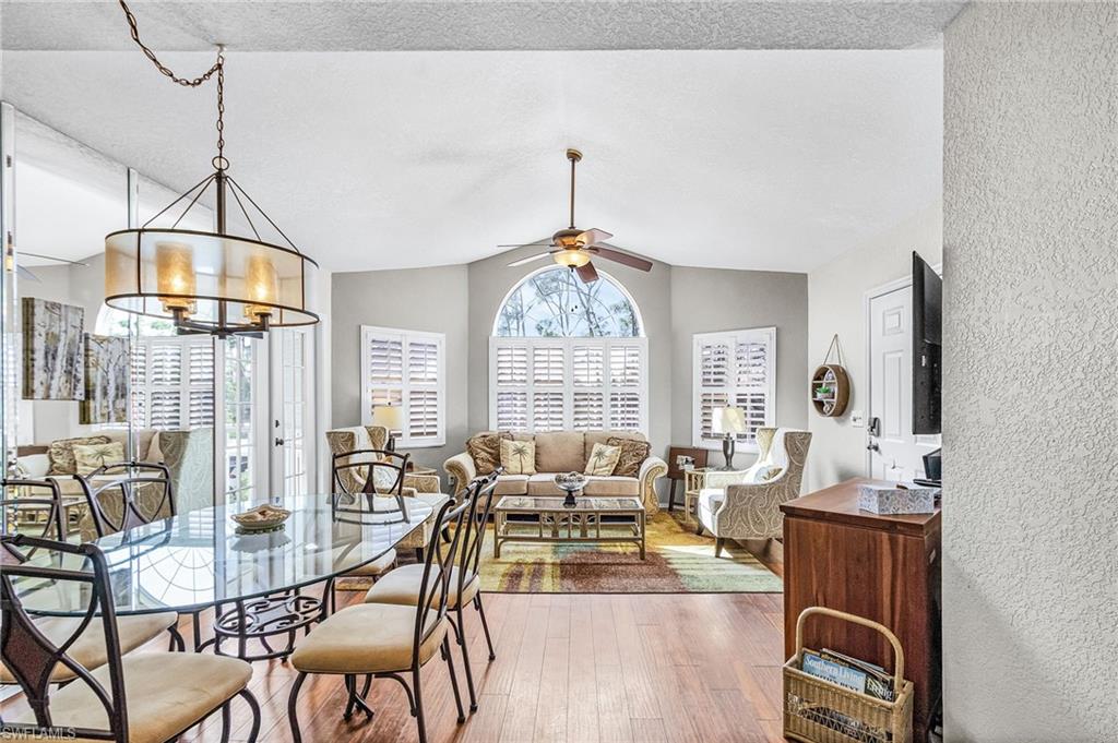 Dining room featuring lofted ceiling, a ceiling fan, wood finished floors, a chandelier, and a textured ceiling