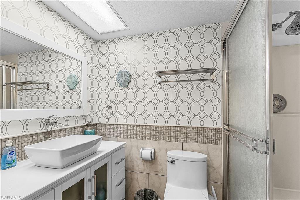 Full bath featuring tile walls, vanity, a stall shower, and a textured ceiling