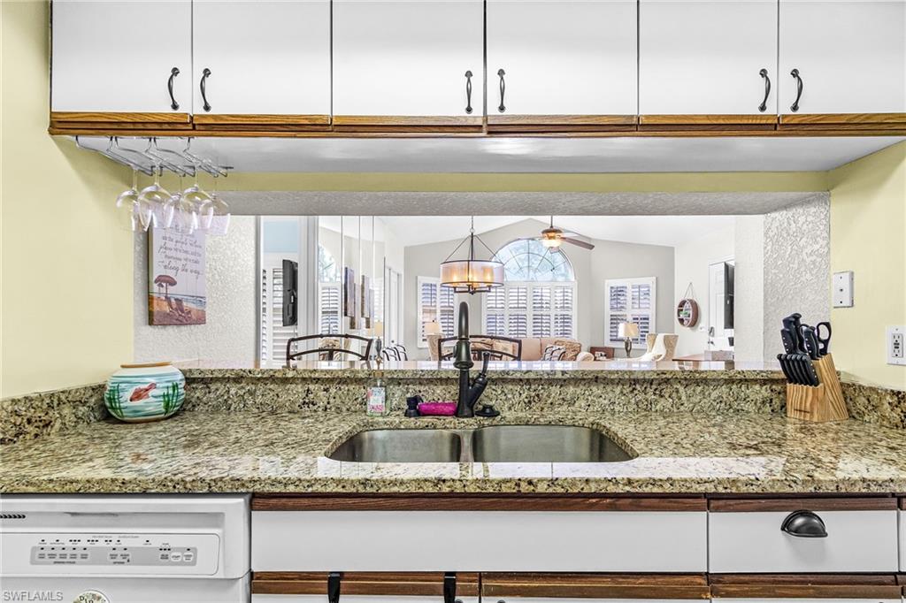 Kitchen featuring light stone countertops, white dishwasher, white cabinets, and a chandelier