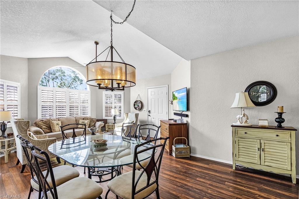 Dining room with a textured wall, lofted ceiling, dark wood-type flooring, a textured ceiling, and a chandelier