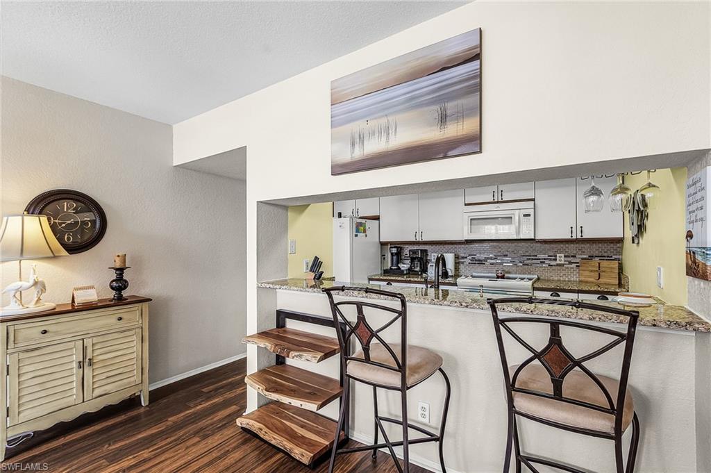 Kitchen with a breakfast bar, white cabinets, light stone counters, white appliances, and dark wood-style flooring