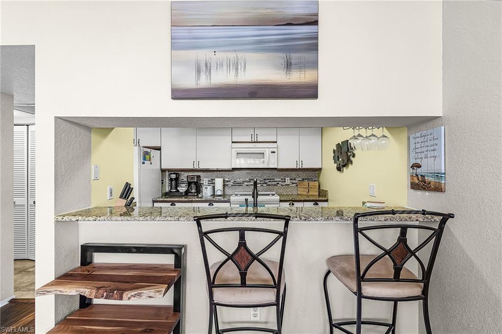 Kitchen featuring a textured wall, light stone counters, white cabinetry, a breakfast bar, and white appliances