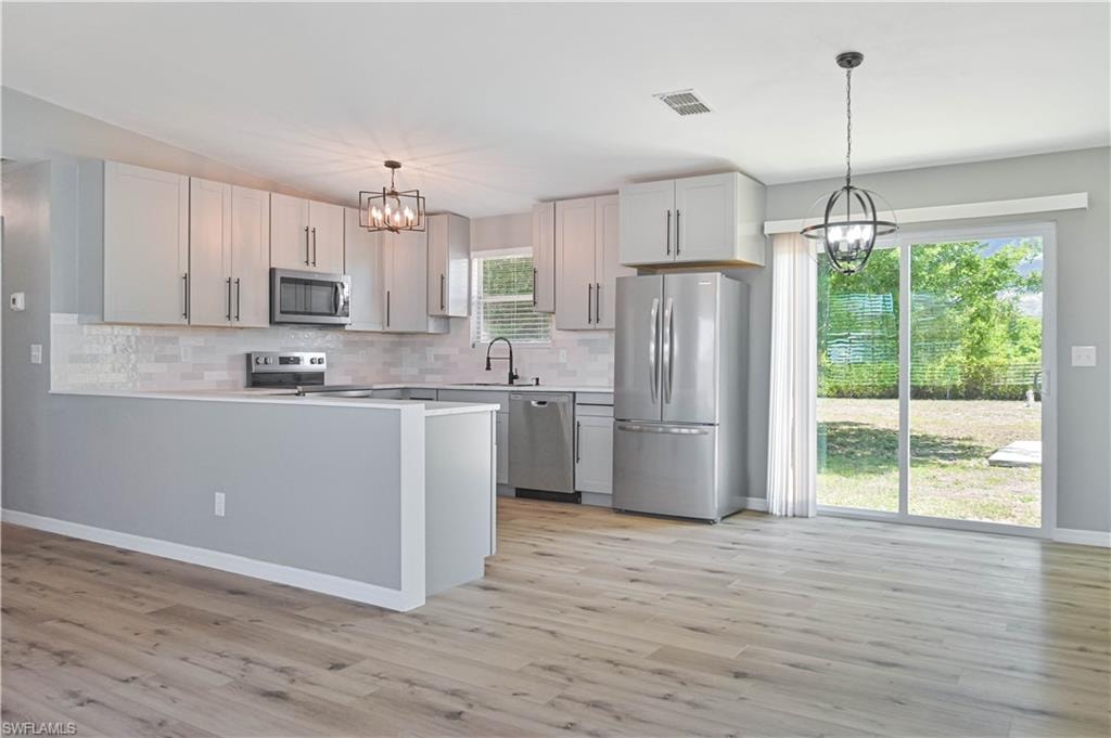 Contemporary kitchen and dining area featuring light wood-finish flooring, light gray cabinetry, stainless steel appliances, and a subway tile backsplash
