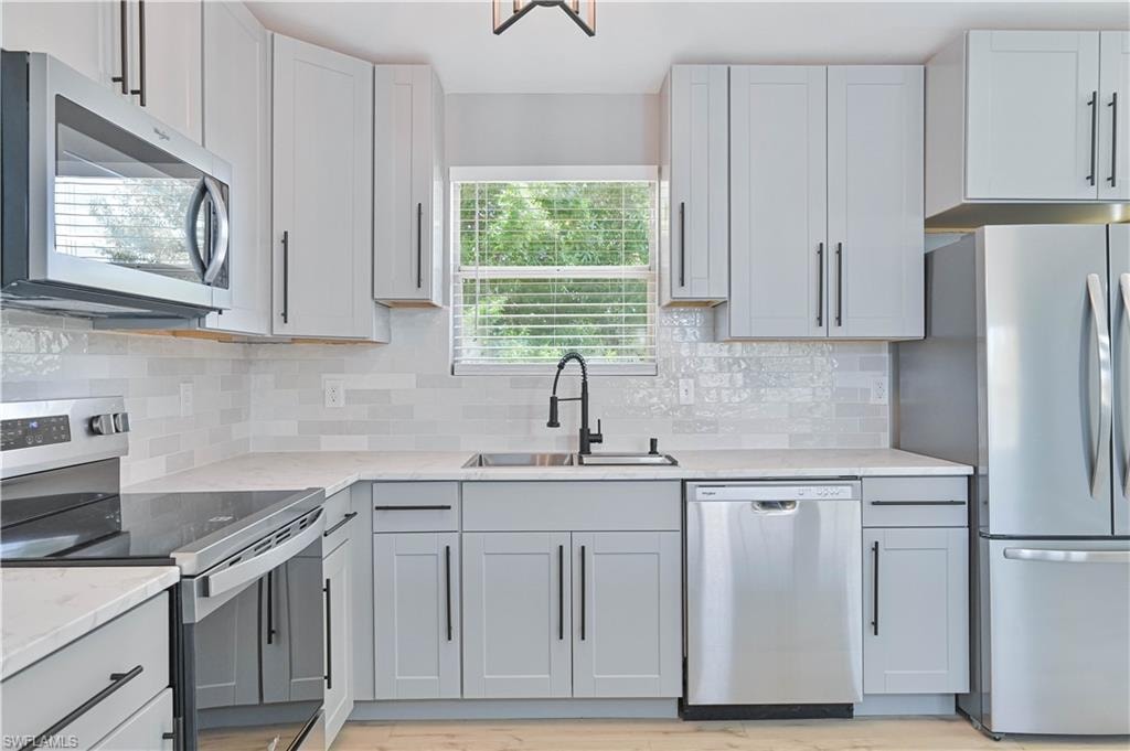 Modern kitchen featuring light gray shaker cabinetry, stainless steel appliances, a white subway tile backsplash, light-toned countertops, and a matte black gooseneck faucet