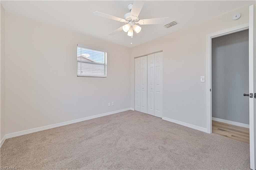 Neutral tone walls featuring carpet flooring, a window with blinds, bi-fold closet doors, and a ceiling fan with integrated lighting