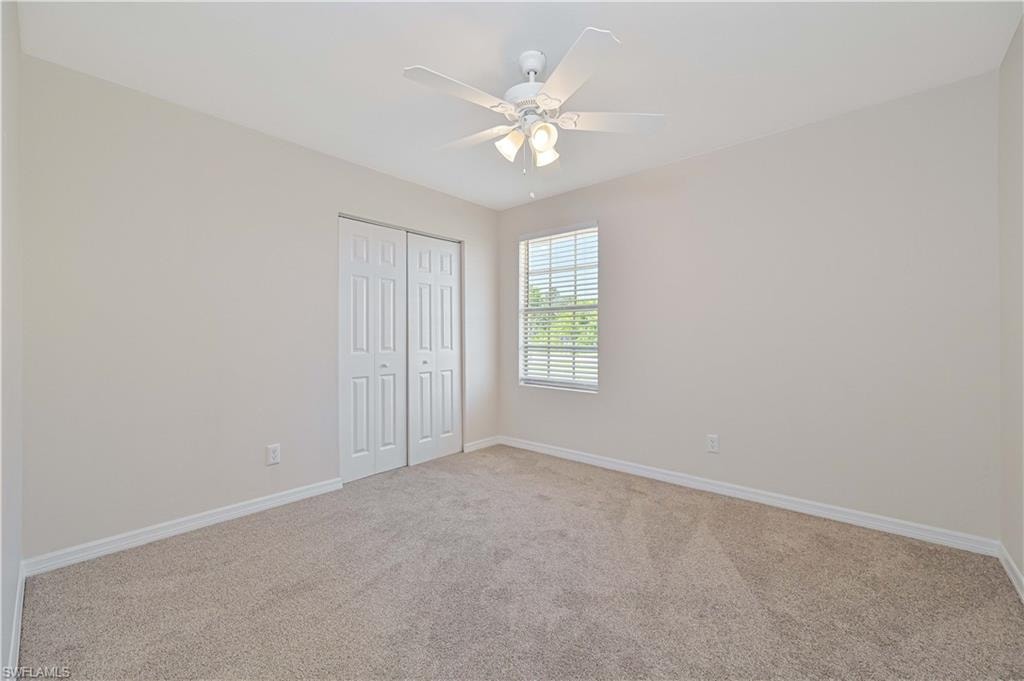Carpeted room featuring a ceiling fan with integrated lighting, a window with horizontal blinds, and bi-fold closet doors