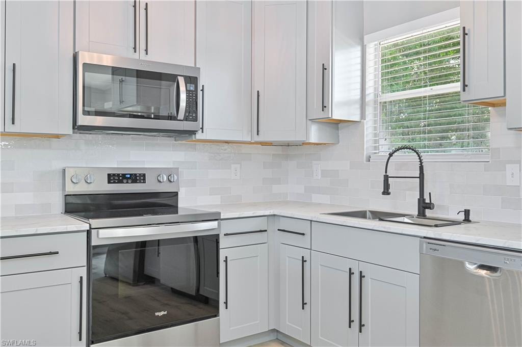 Modern kitchen featuring light gray cabinetry with black hardware, white quartz countertops, a white subway tile backsplash, and stainless steel appliances