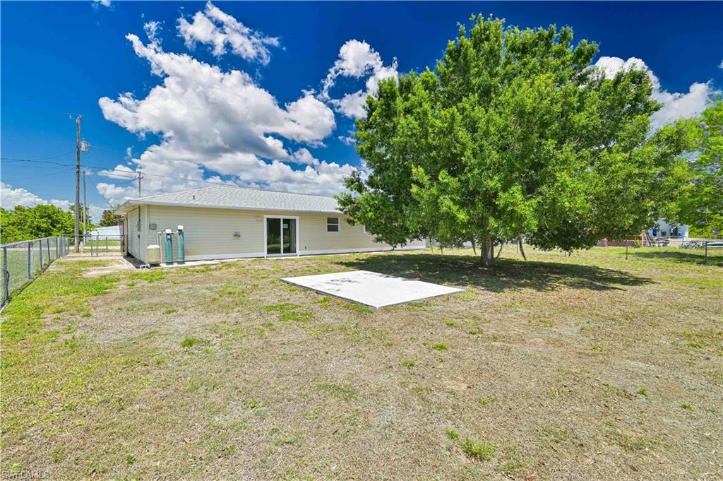 Expansive yard with mature tree providing natural shade, a concrete patio, and full perimeter chain-link fencing