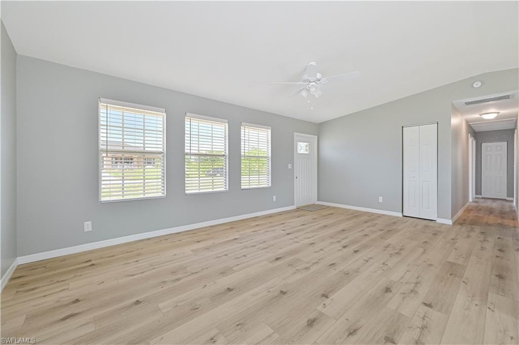Spacious living area featuring light wood-finish flooring, three windows with blinds, and a white ceiling fan