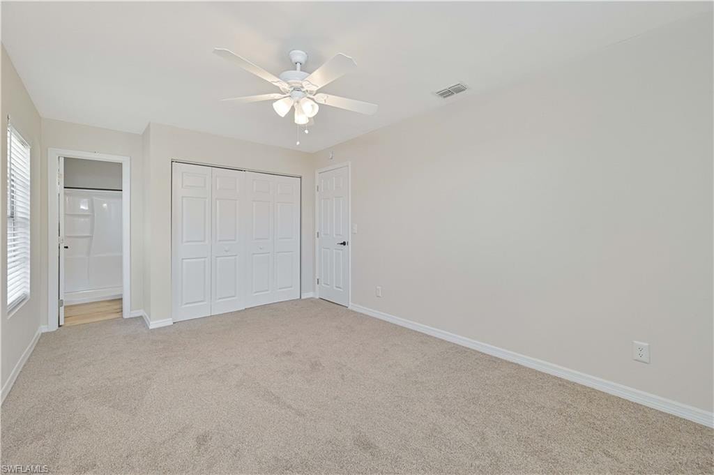 Carpeted room featuring a ceiling fan with light fixture, white bi-fold closet doors, and an open doorway to a bathroom with a white shower/tub combo